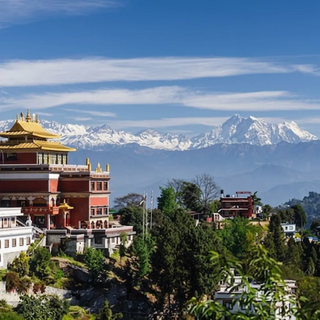 Ornate red and gold Tibetan Buddhist monastery on a hillside with snow-covered Himalayan peaks behind.