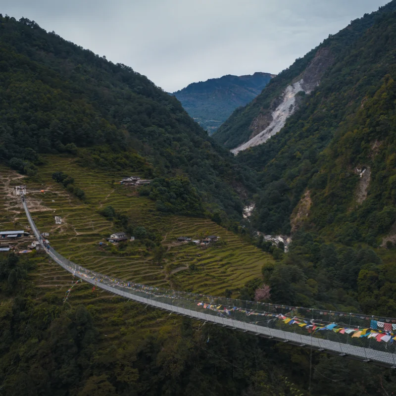 Extremely long steel suspension footbridge decorated with prayer flags spanning a deep mountain gorge near Jhinu Danda Nepal.