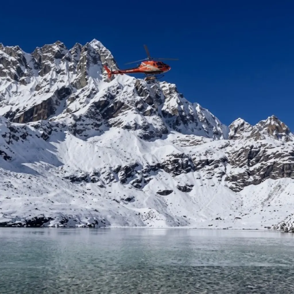 Orange tour helicopter flying over the tranquil waters of a high-altitude glacial lake and snowy peaks