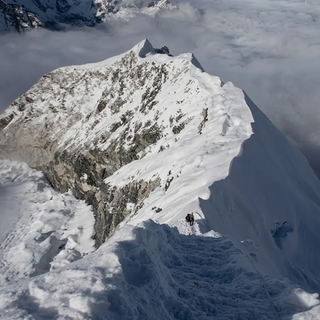 Climber navigating a sharp snowy ridgeline above clouds on a high-altitude Himalayan mountain peak.