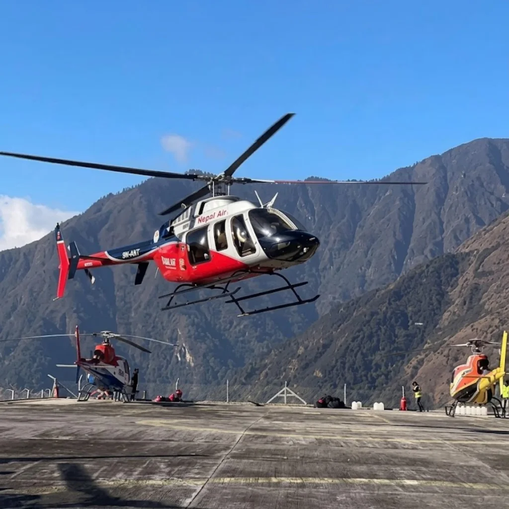 Red and white Nepal Air helicopter taking off from a busy mountain helipad against steep green ridges.