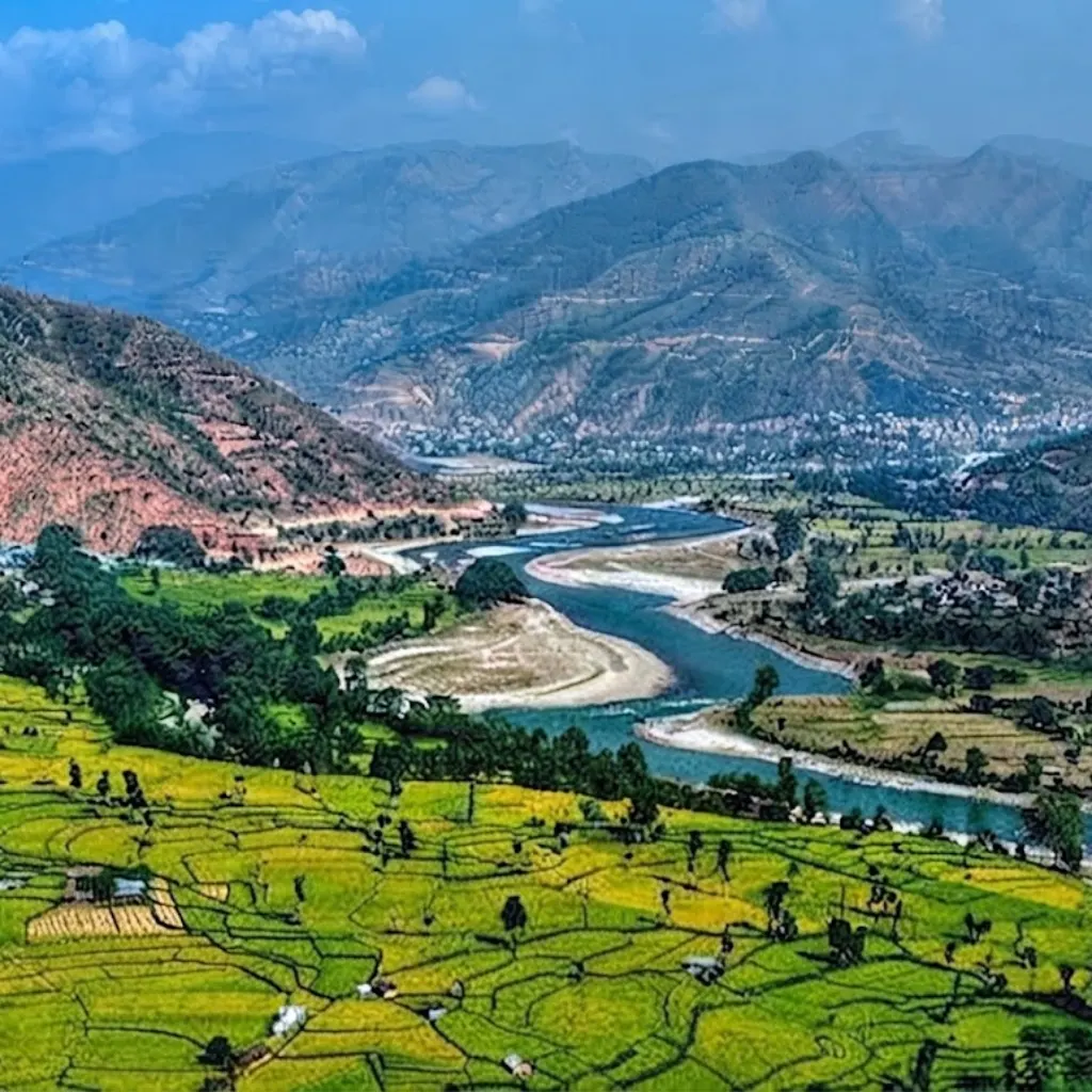 Winding blue river flowing through verdant terraced farm fields and rural foothill settlements bordered by rolling green mountains.