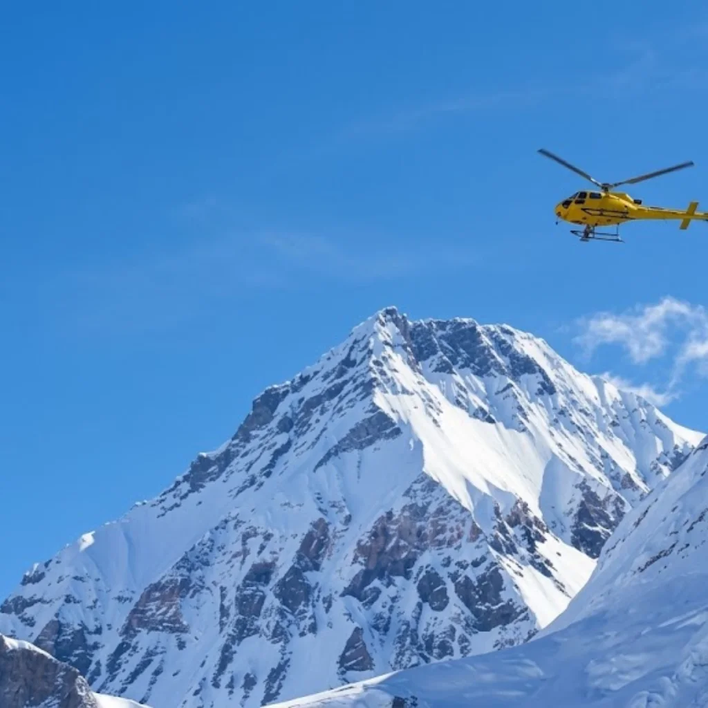 Yellow rescue helicopter soaring past sheer snow-covered rock faces into clear blue Himalayan skies in Nepal.