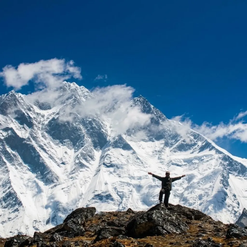 Trekker standing on a rocky hill with arms outstretched in front of the massive snowy face of Lhotse.