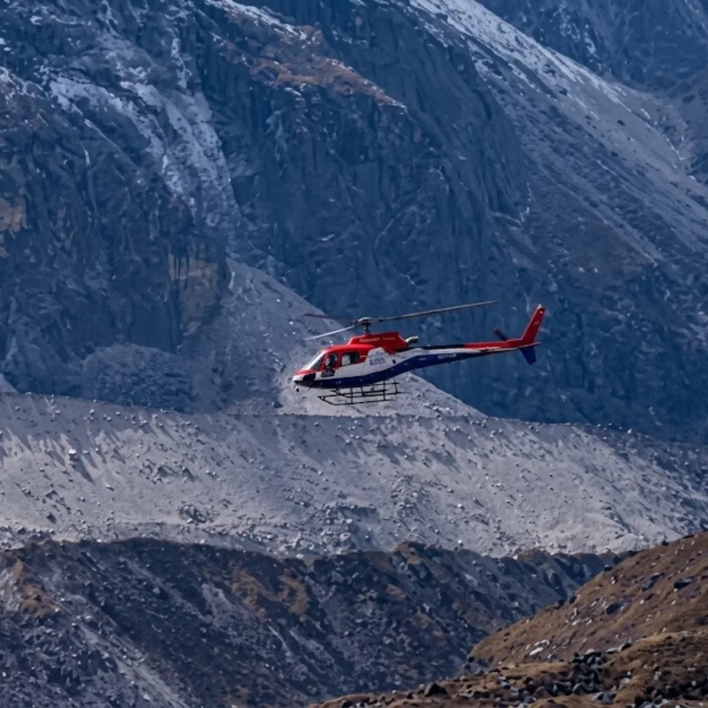 Red and blue helicopter flying across a high-altitude rocky mountain valley and scree slopes in the Khumbu.