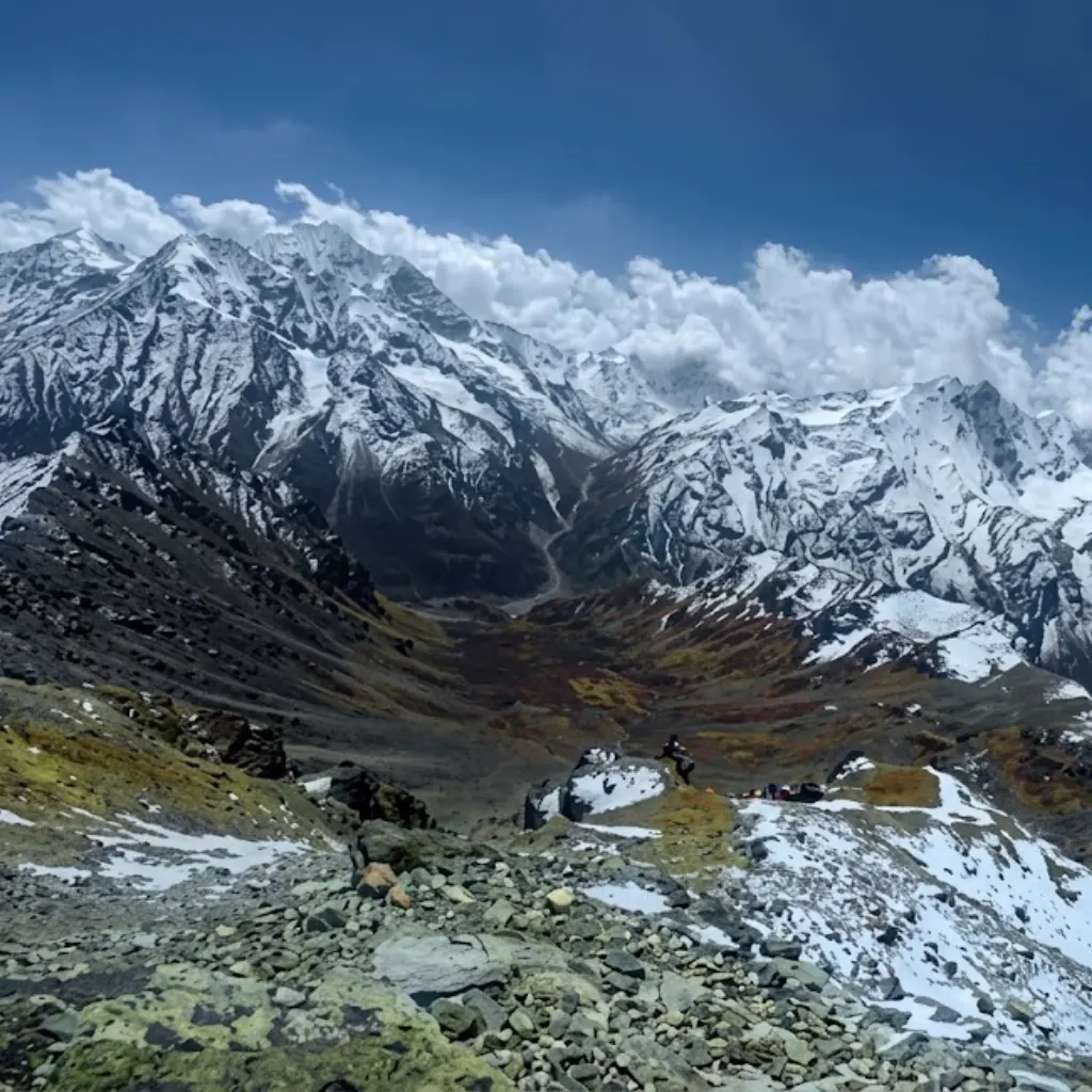 Hiker resting on a rocky ridge overlooking a deep mountain valley and snow-covered Himalayan mountain range.