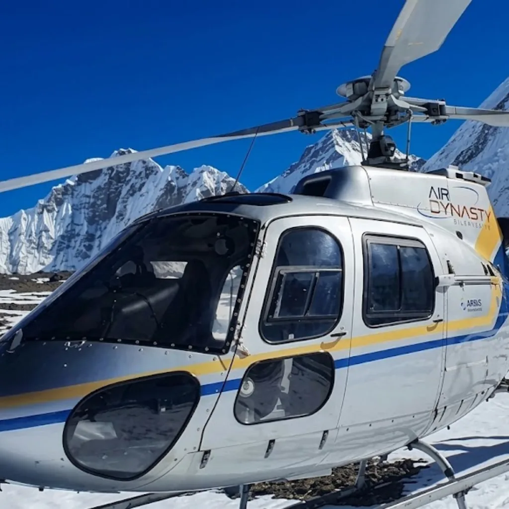Air Dynasty charter helicopter cockpit parked on a snowfield before jagged glaciated mountain walls.