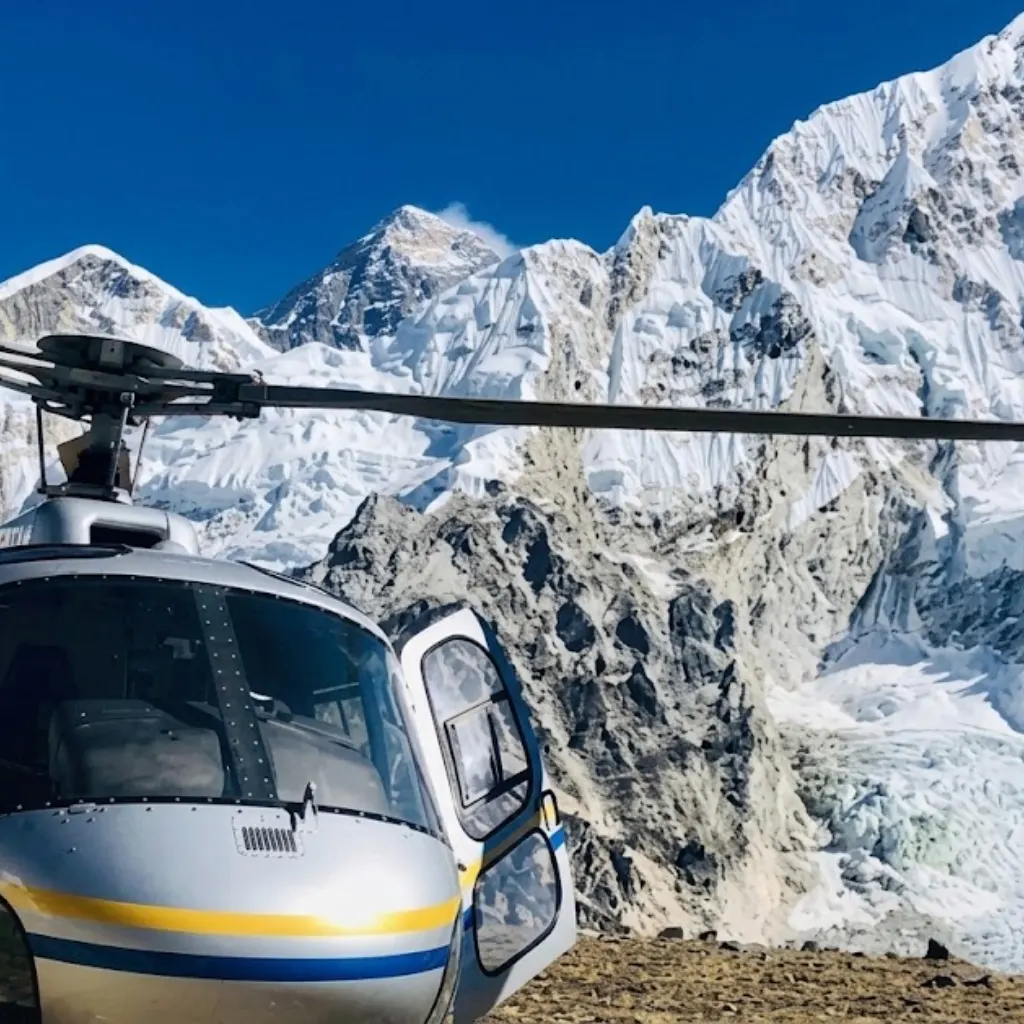 Helicopter cockpit parked on an alpine ridge facing Mount Everest and glaciated Himalayan mountain faces.