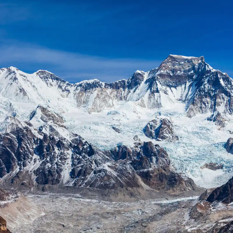 High-altitude cliffside village shrouded in morning mist and woodsmoke with snowy mountain peaks in Mustang Nepal.