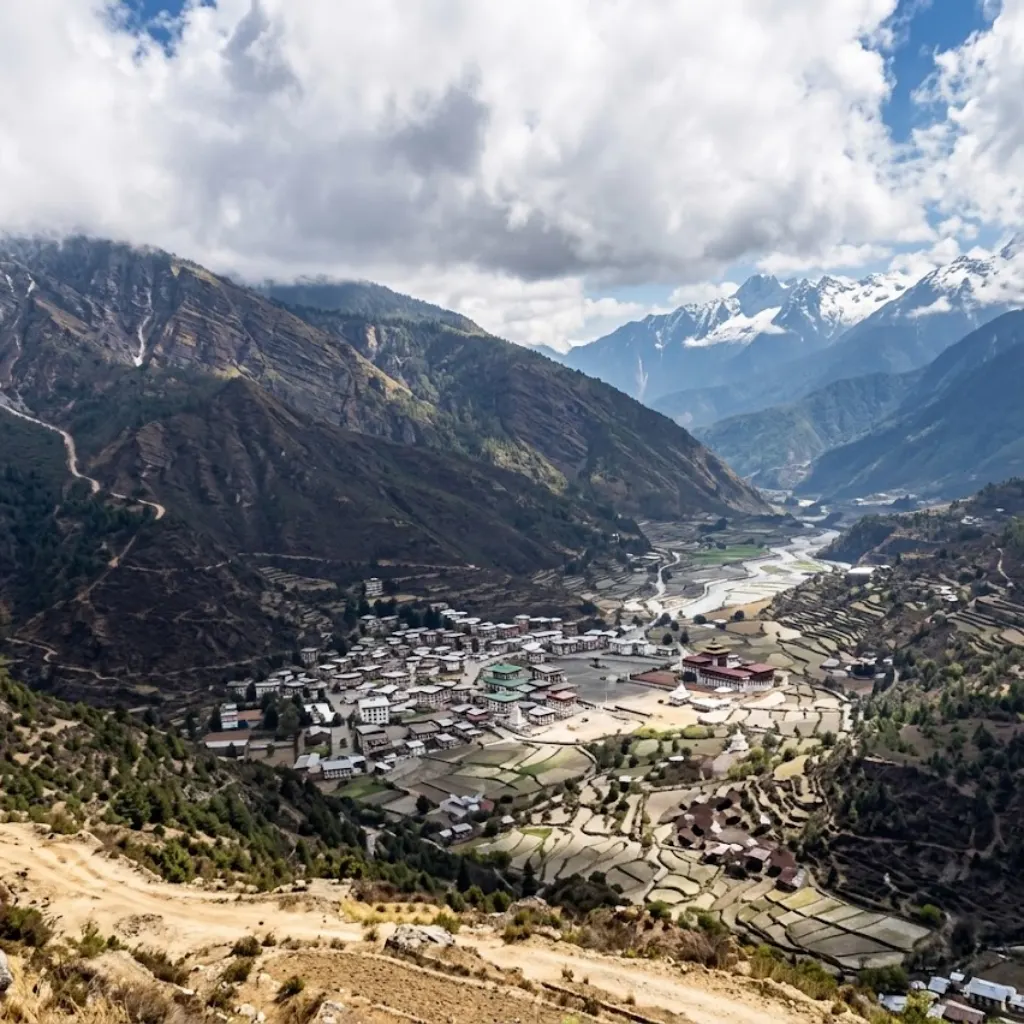 Elevated landscape view overlooking Lukla town, its airstrip, and the deep forested Dudh Koshi river valley beneath sunlit mountain clouds.