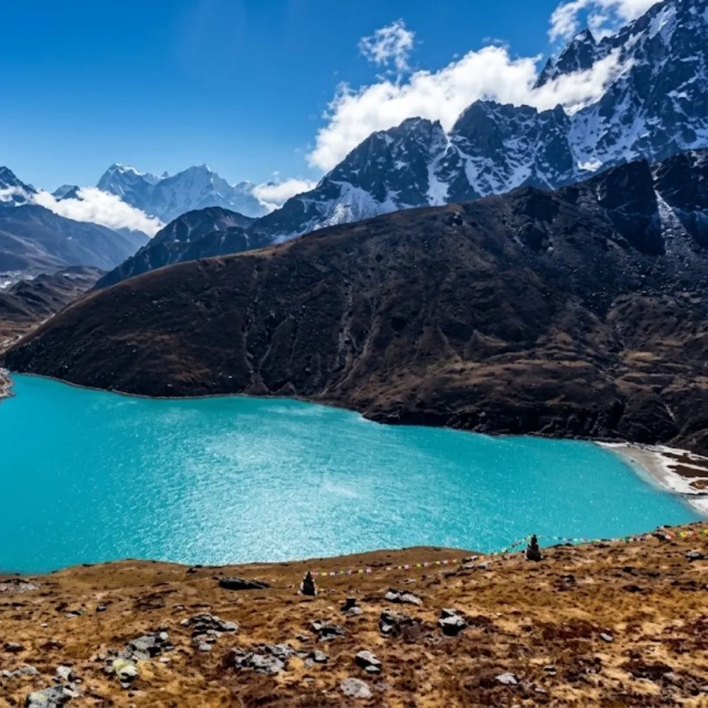 Vibrant turquoise waters of Gokyo Lake surrounded by brown alpine ridges beneath dramatic snow-capped peaks.