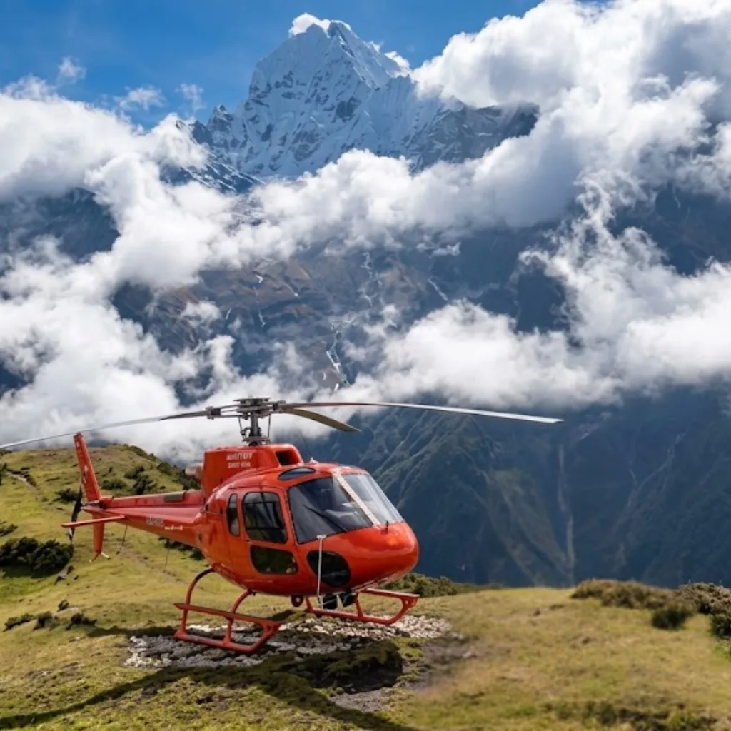 range tour helicopter parked on a grassy alpine ridge facing cloud-shrouded Mount Ama Dablam in Nepal.