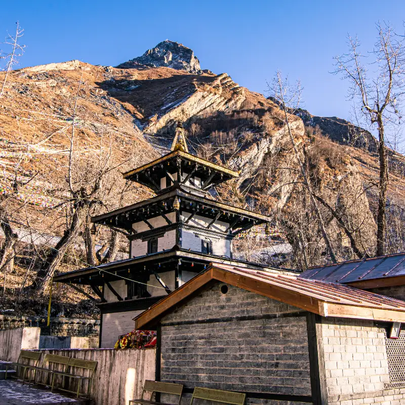 Multi-tiered pagoda-style Muktinath temple with stone walls set against steep, rugged mountain slopes.