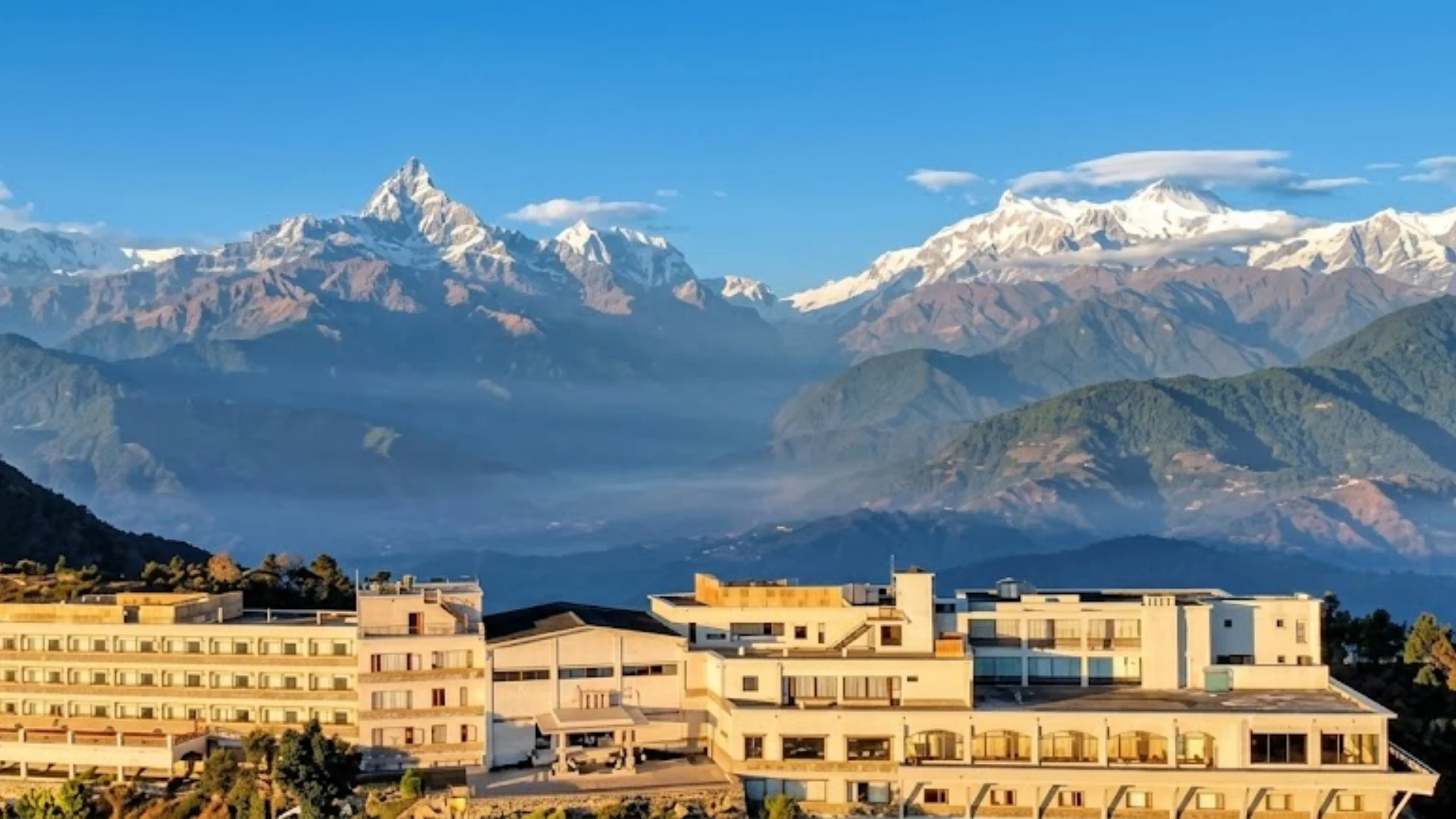 Panoramic view of Sarangkot resort overlooking misty valleys and snow-covered Mount Machapuchare.