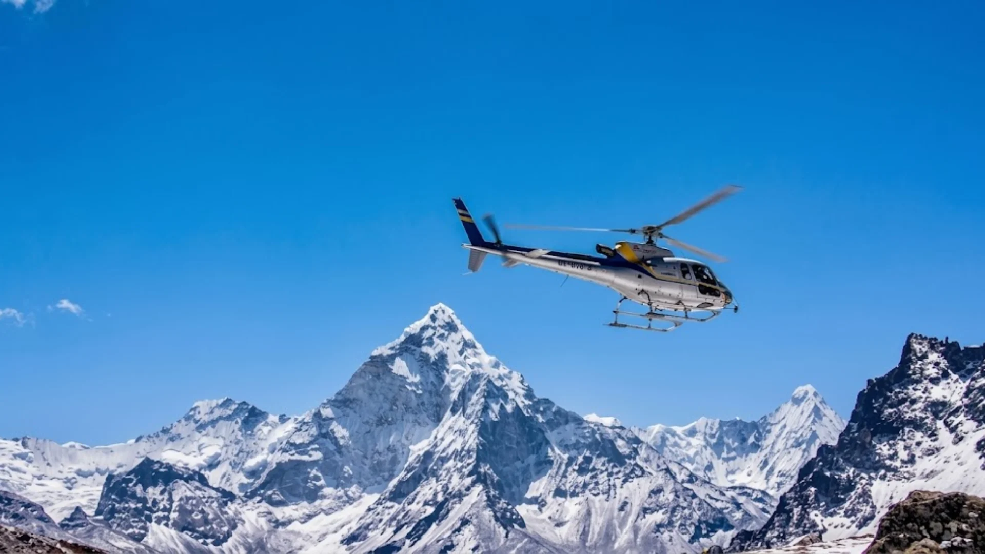 Silver and blue tour helicopter flying against a clear sky past snow-covered Mount Ama Dablam in Nepal